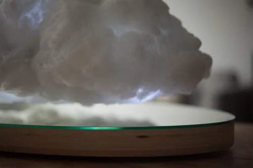 Alto falante em formato de nuvem branca iluminada por levitação magnética sobre base circular de madeira.