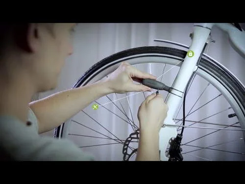 Instalando sistema de luz e ímãs na bicicleta branca. Mãos ajustam acessório na forquilha e roda dianteira.