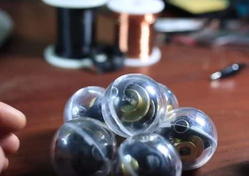 Brinquedo nanodot gyro com imas de neodimio: Grupo de esferas transparentes com discos dourados e elementos escuros internos sobre mesa, mão ao lado.