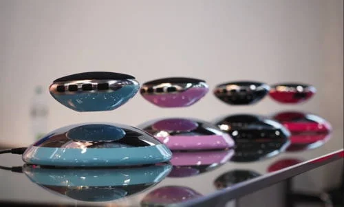 Caixas de som flutuantes bluetooth, em azul, rosa, preto e vermelho. Alguns modelos levitam, outros estão sobre bases refletoras.