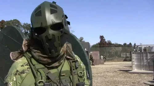 Pessoa com capacete tático verde militar, estilo Star Wars e camuflado, em campo aberto. Design lembra Exército Americano.