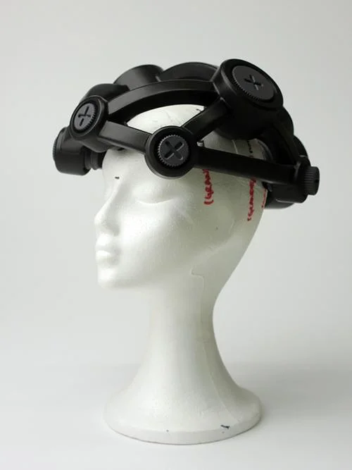 Capacete magnético preto para enxaqueca/parkinson, com elementos circulares ajustáveis, em manequim branco.
