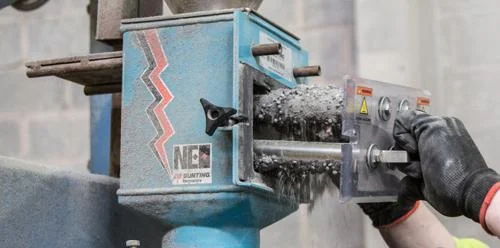 Separador magnético Bunting Neo azul processa granulados cinza. Mão com luva opera para Ecovyn reduzir desperdício.