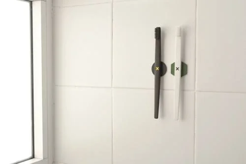 Escovas de dente com imãs: uma preta e uma branca, fixadas verticalmente em parede de azulejos brancos.