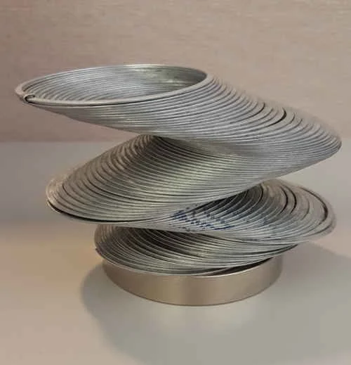 Escultura surpreendente de anéis metálicos finos prateados empilhados e torcidos magneticamente sobre base cilíndrica.