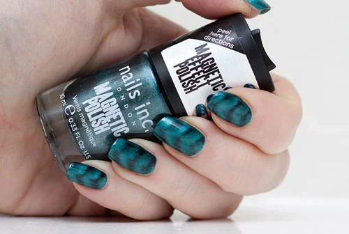 Esmaltes magnéticos Nails Inc azul-petróleo em frasco, e nas unhas com padrão ondulado.