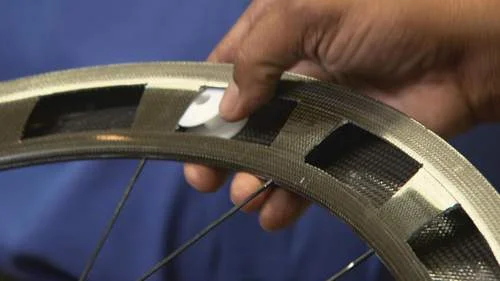 Imã escondido para fraude no ciclismo. Mão insere ímã oval branco no aro de carbono da bicicleta.