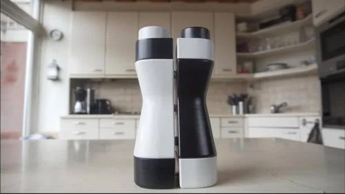 Duas garrafas de água magnéticas, uma branca e uma preta com design ergonômico, em balcão de cozinha.