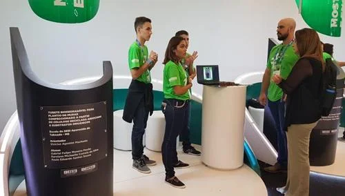 Tubete Biodegradável para Plantio, feito de celulose reciclada, apresentado em estande com pessoas e laptop exibindo detalhes.