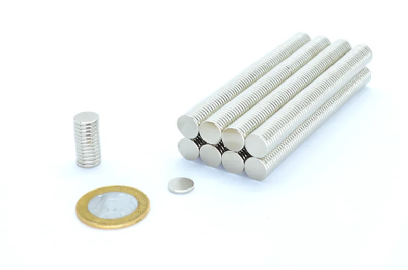 Ímã de neodímio 10x1.5mm. Pilha vertical, barra de discos alinhados, e um disco avulso. Moeda R$1 para escala.