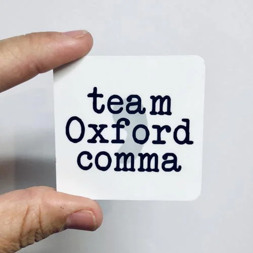 Ímã de geladeira para quem ama livros: quadrado branco com team Oxford comma em preto, segurado por dedos.