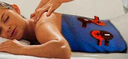 Sessão de magnetoterapia e terapia dos imãs. Mulher recebe massagem, com eletrodos de polaridade (+/-) em almofada azul nas costas.