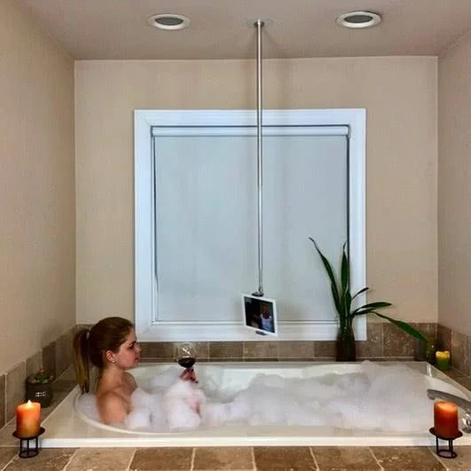 Skyfloat: alça magnética para o teto, um mastro prateado suspende um tablet sobre banheira. Mulher em espuma, vinho e velas.