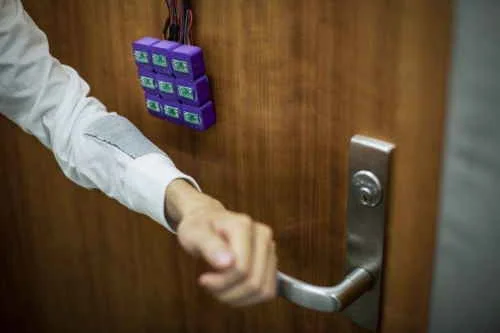 Tecido magnético, parte de tecnologia com módulos roxos em porta de madeira, enquanto mão segura a maçaneta para abrir.