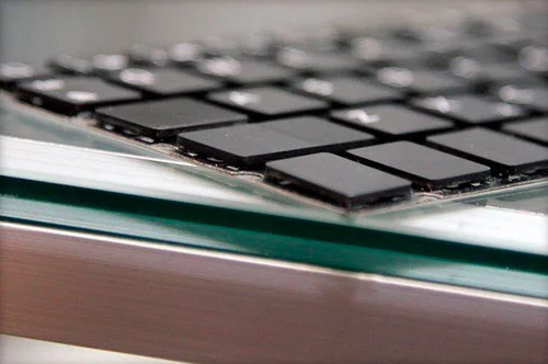 Teclas pretas retangulares finas de um teclado com tecnologia maglev, dispostas em grade sobre vidro. Novidade da informática.