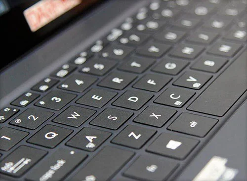 Teclado de notebook preto em close-up, com teclas brancas QWERTY. Peça chave na informática atual.