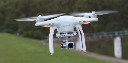 Drone branco, tecnologia de quatro hélices com câmera, flutuando sobre gramado.