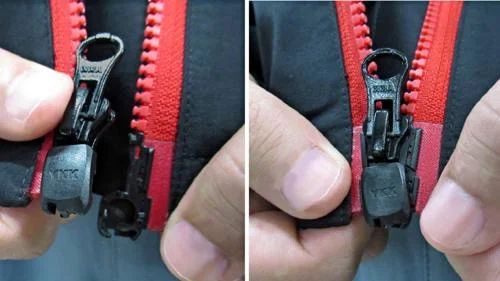 Zíper magnético YKK preto sendo engatado e travado por uma mão. Detalhe do zíper vermelho em jaqueta escura.